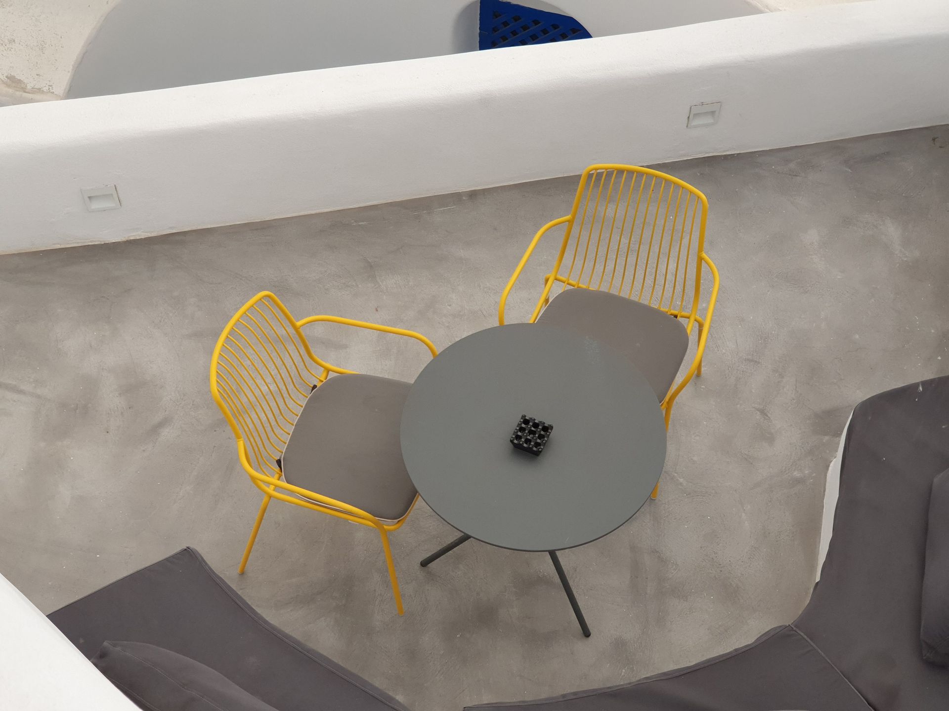 Top view of a minimalistic outdoor seating area with yellow chairs and a round table.